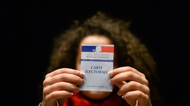 Une femme montre sa carte électorale, en France. On peut y lire : « Liberté, égalité, fraternité. La République française ».