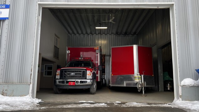 Un camion et une remorque sont stationnés dans un garage dont la porte ouverte.