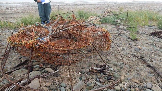 Un casier rouillé pour la pêche au crabe des neiges est examiné par un homme sur une plage. Un casier rouillé pour la pêche au crabe des neiges est examiné par un homme sur une plage.