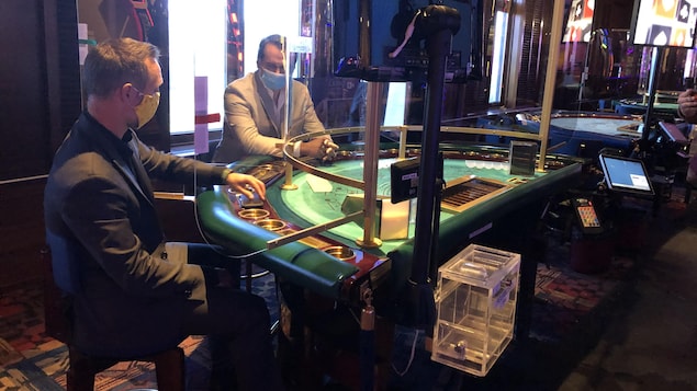 Deux hommes avec des masques installés à une table de jeux dans un casino.
