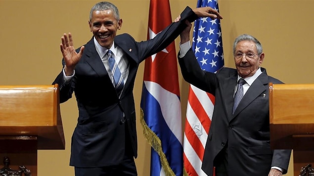 Le président cubain soulève le bras gauche de son homologue américain en lui tenant le poignet.