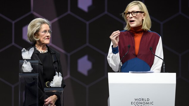 Cate Blanchett s'exprime sur une scène, derrière un lutrin. Cate Blanchett s'exprime sur une scène, derrière un lutrin.