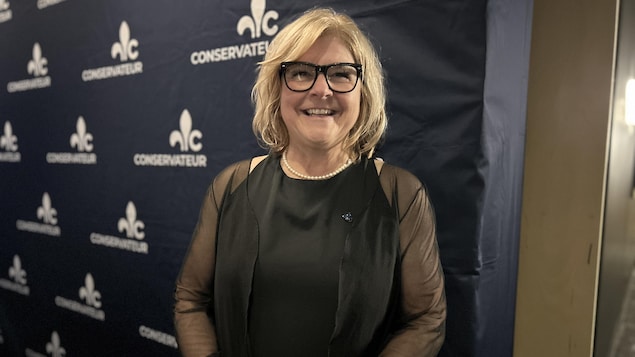 Catherine Morissette sourit devant une affiche du Parti conservateur du Québec.