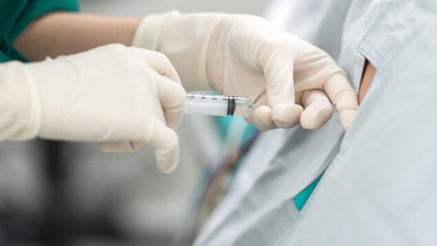 Une anesthésiste fait une injection dans le dos d'une personne avec un cathéter épidural.