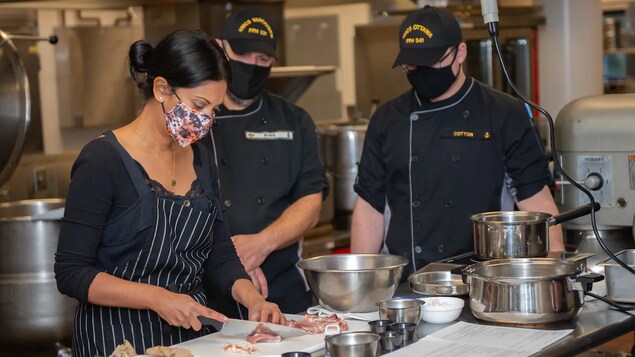 Ruwanmali Samarakoon-Amunugama pointe vers des pièces de viande devant deux militaires dans une cuisine commerciale.