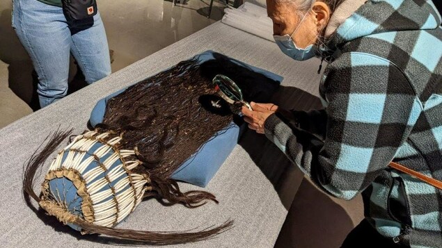 La cheffe héréditaire de Maiyoo Keyoh, Petra A'Huille, examine à la loupe une coiffure faite de coquillages et de tresses de cheveux qui a appartenu à son arrière-arrière-grand-père, George A'Huille, à Prince George, en Colombie-Britannique, à l'automne 2022.