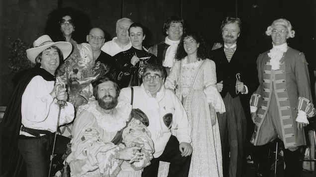 L'équipe de CBF Bonjour posant avec des costumes de théâtre. Agenouillés devant l'objectif: Roger "Cyrano" Laroche, Joël "Roméo" Le Bigot et Paul Buissonneau. Debout: Francine "Roxane, Juliette" Grimaldi, Jean-Louis Millette, Raymond "le souffleur" Lebrun, Louise-Renée "Christian" Bessette, André "Petruchio" Croteau, Ève "Catharina" Christian, Le Dr Marc "Knock" Laurendeau.
