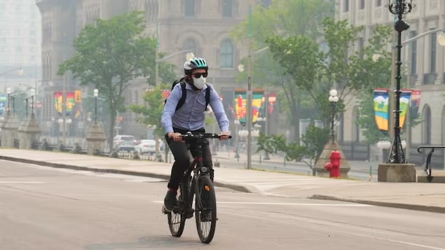 A cyclist wears a mask during poor air quality conditions as smoke from wildfires in Ontario and Quebec hangs over Ottawa on Tuesday.
