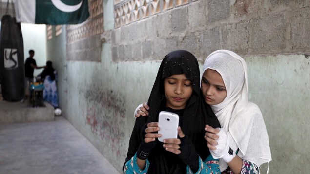 Deux jeunes Pakistanaises portant le voile regardent le même téléphone cellulaire blanc. Deux jeunes Pakistanaises portant le voile regardent le même téléphone cellulaire blanc.