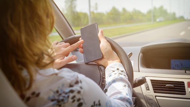 Une femme utilise un téléphone cellulaire appuyé sur son volant pendant qu'elle conduit une voiture.