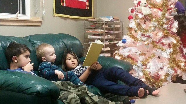 Trois enfants lisent un livre sur un divan. Trois enfants lisent un livre sur un divan.