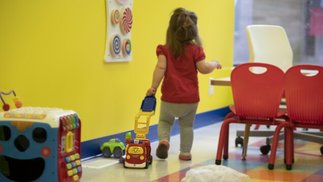 Une enfant vue de dos transporte un jouet dans ses mains.