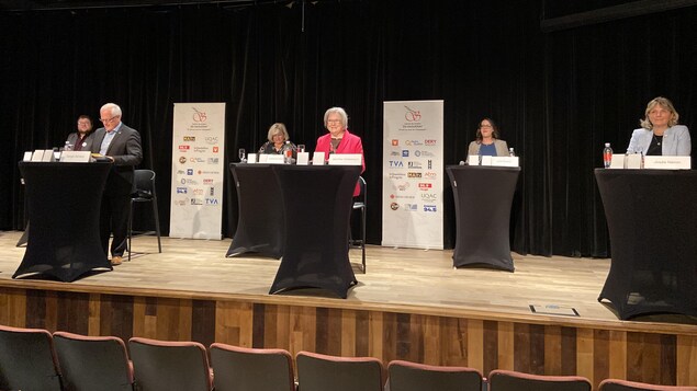 Les candidats à la mairie de Saguenay derrière des lutrins sur scène.