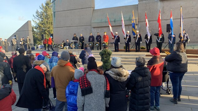 Des gens sont rassemblés devant des dignitaires et des drapeaux, devant le monument commémoratif pour l'explosion d'Halifax.