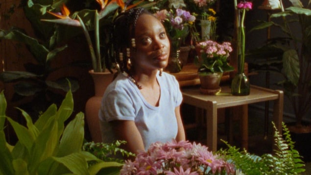 Une jeune fille est assise au milieu de plantes et de fleurs à l'intérieur.