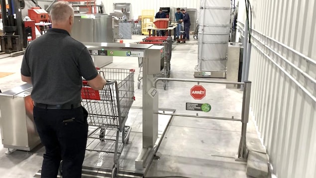 Un homme pousse un panier d'épicerie dans le robot désinfectant. 