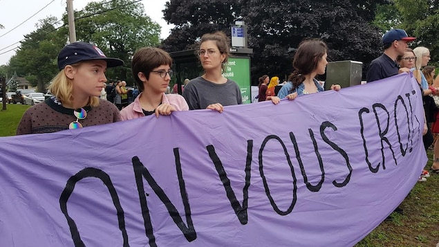 Des manifestants tiennent une banderole en appui aux victimes sur laquelle il est écrit : « On vous croit ». Des manifestants tiennent une banderole en appui aux victimes sur laquelle il est écrit : « On vous croit ».