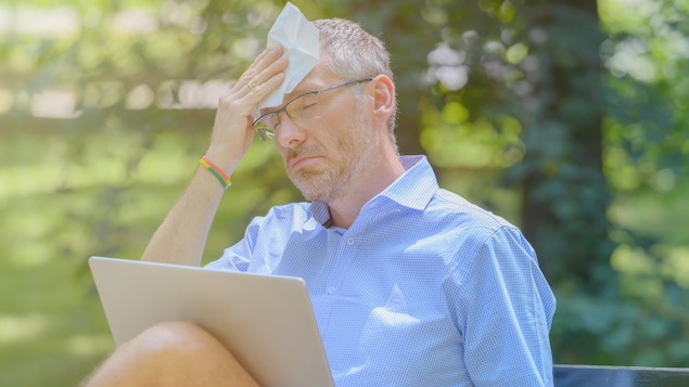 L'homme souffre de chaleur en travaillant avec un ordinateur portable dans le parc et en s'essuyant le front avec un mouchoir en papier.