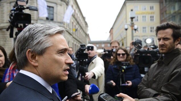 Le ministre est entouré de caméras et de micros.