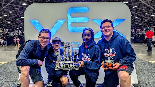 Un homme et trois adolescents sourient en montrant fièrement leur robot et une manette.