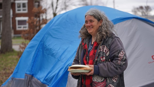 Chantal devant sa tente. avec un morceau de pizza dans les mains, dans un parc.