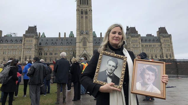 Chantal Jacob devant le Parlement à Ottawa avec des photos encadrées de ses parents.