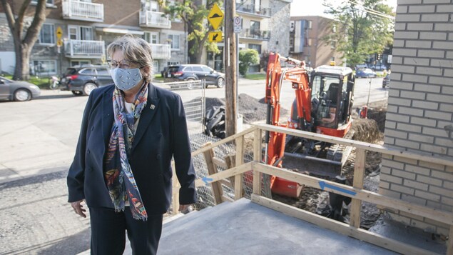 Chantal Rouleau, portant un masque, dehors à l'entrée d'une école avec, derrière elle, une tractopelle.