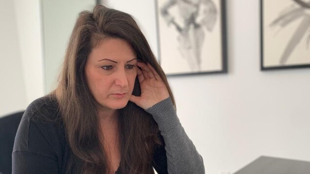 Chantale Renaud, assise à sa table de cuisine, regarde l'écran de son ordinateur portable et a les doigts de la main gauche posés sur sa tempe.