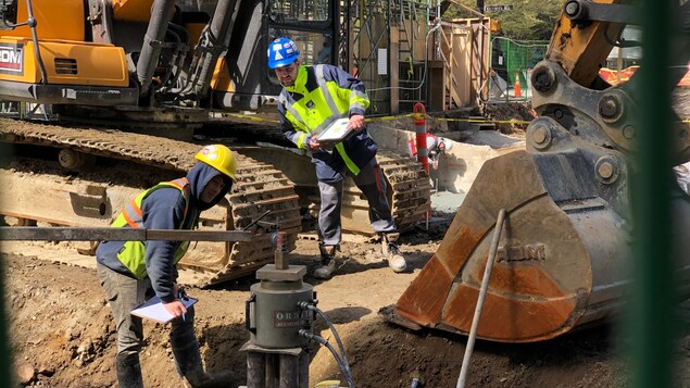 Deux ouvriers se tiennent à une certaine distance l'un de l'autre, aux côtés d'un bulldozer.