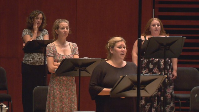 Des femmes chantent. Un pupitre est installé devant chacune d'elles.