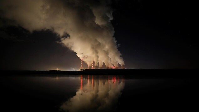 La centrale au charbon de Belchatow, la nuit, sous l'imposante masse de fumée qui s'échappe de ses cheminées et qui se reflète sur un cour d'eau voisin.