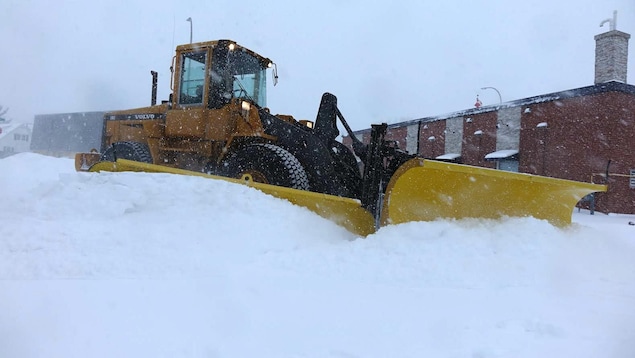 Un chasse-neige dégage un terrain de stationnement enneigé
