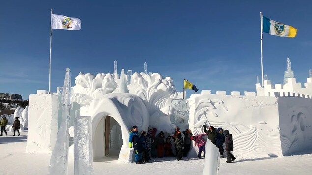 Sous un ciel bleu, des gens sont debout à côté du chateau de neige du Festival d'hiver Snowking