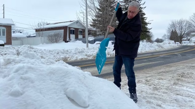 Un homme pique une pelle dans un banc de neige.