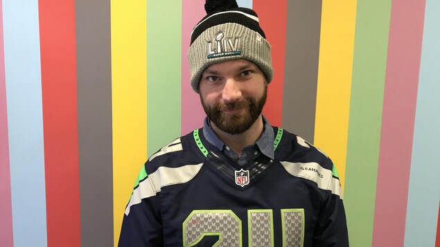 Un homme blanc avec la barbe et un bonnet et un maillot de football. 