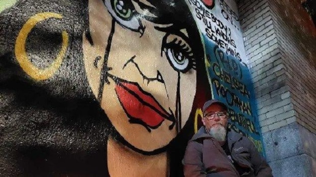 Un homme pose devant une peinture murale.