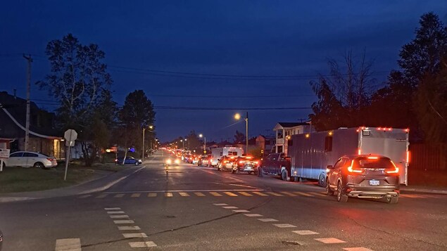 Des voitures en file qui quittent la ville de Chibougamau en soirée. 