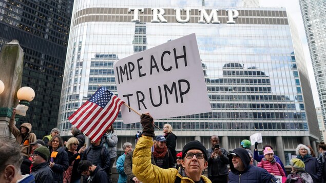 Des gens manifestent devant un immeuble sur lequel est inscrit le nom «Trump».