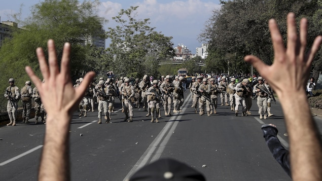 Un manifestant lève les mains devant des soldats qui avancent vers lui.