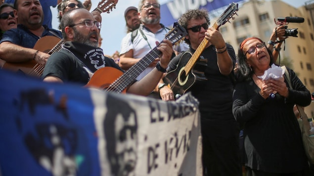 Des hommes jouent de la guitare derrière un drapeau qui sert de banderole dans une manifestation.