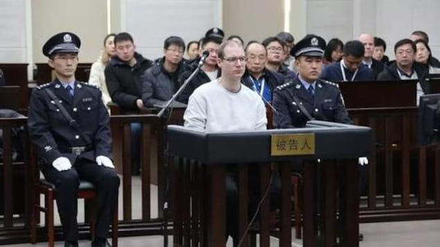 Un homme est assis dans le box des accusés flanqué de deux policiers chinois.