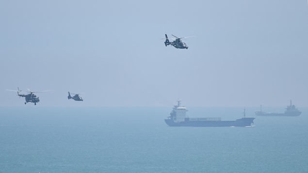 Des hélicoptères volent au-dessus de la mer, où se trouvent des navires.
