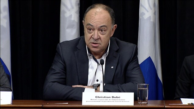Christian Dubé, lors d'une conférence de presse, est assis derrière une table. Il parle dans un micro.