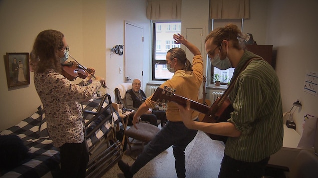 Deux musiciens et un danseur qui font une prestation devant Roland Vandal assis dans un fauteuil.