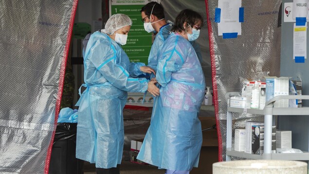 Une travailleuse attache le dos de la blouse en plastique d'une de ses consœurs.
