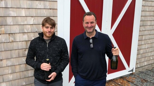Deux personnes qui tiennent chacun une bouteille de cidre.