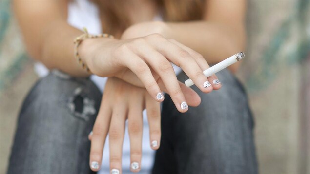 Une adolescente tient une cigarette entre ses doigts.