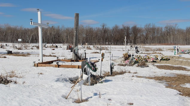 Un cimetière sous la neige, on voit quelques croix et quelques fleurs.