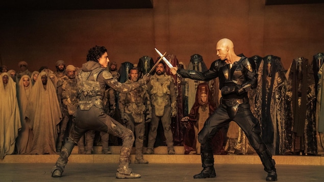 Deux hommes brandissant des épées se faisant face à face devant un public.