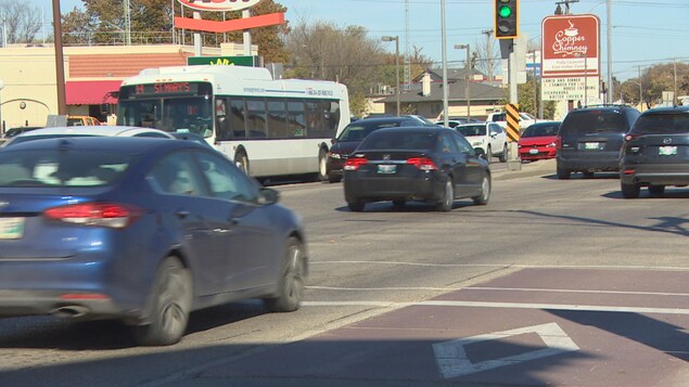Des voitures roulent dans les deux sens sur une avenue à trois voies de chaque côté. On voit également un autobus. Des voitures roulent dans les deux sens sur une avenue à trois voies de chaque côté. On voit également un autobus.